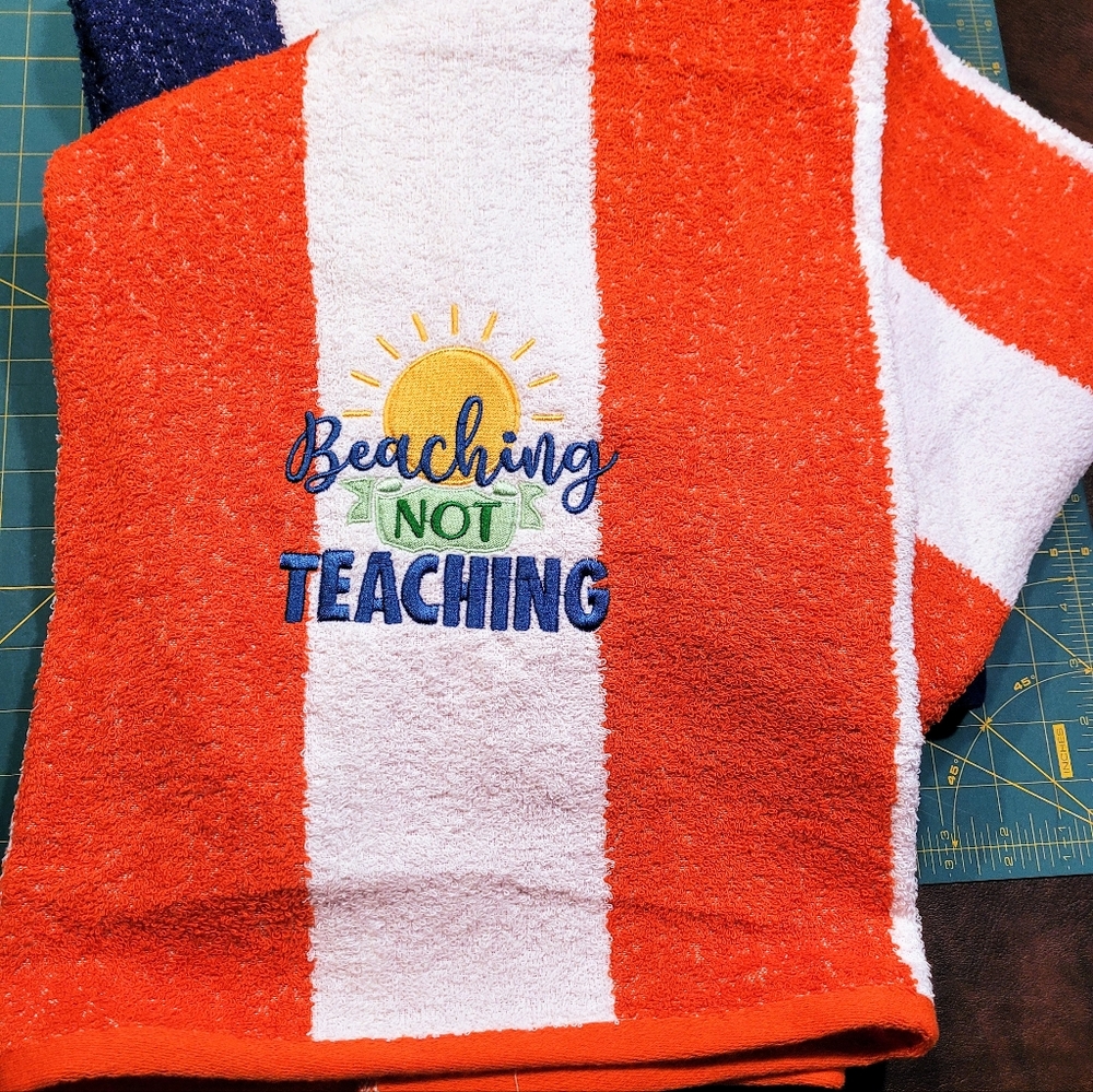Beach towel with "Beaching Not Teaching" embroidery. Orange and white striped